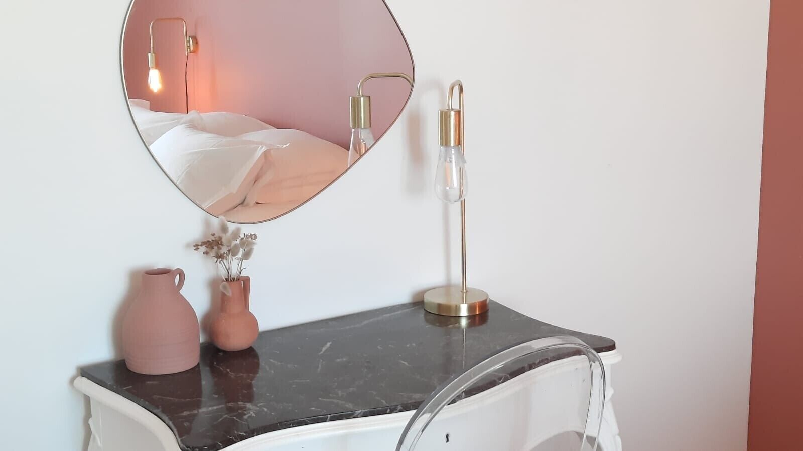 Een wastafelmeubel met een spiegel, een vaas met gedroogde bloemen en een lamp.