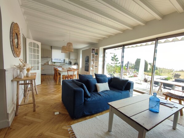 Un salón moderno con un sofá azul, suelo de madera y un amplio ventanal corredero que da a un patio exterior.