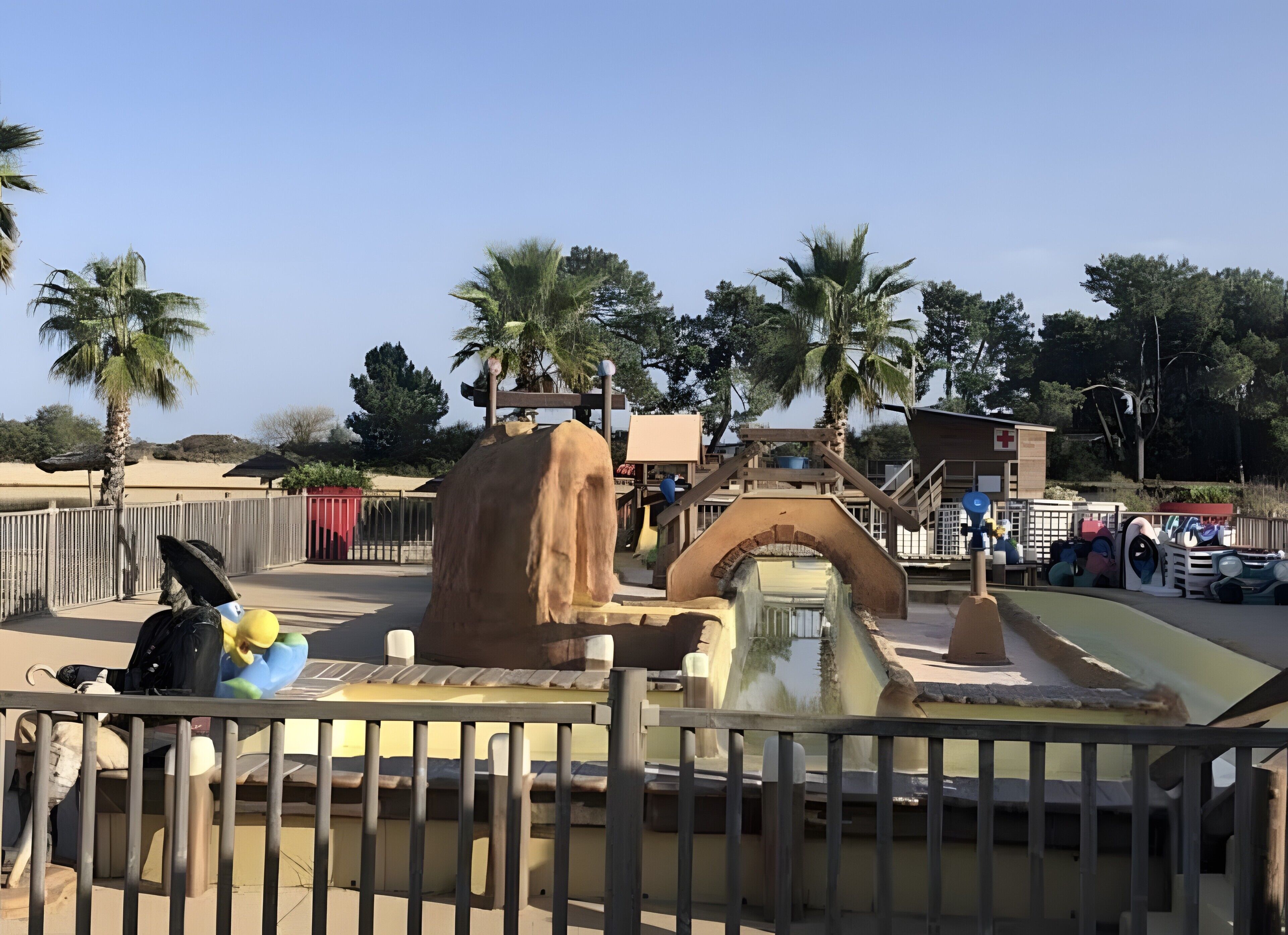 A water feature with a waterfall, palm trees, and a fenced area.