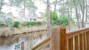 A wooden deck with a river, surrounded by trees and a row of mobile homes. - The Bassin Cabin – 3-Bedroom Mobile Home with Terrace and Pool (Lège-Cap-Ferret)