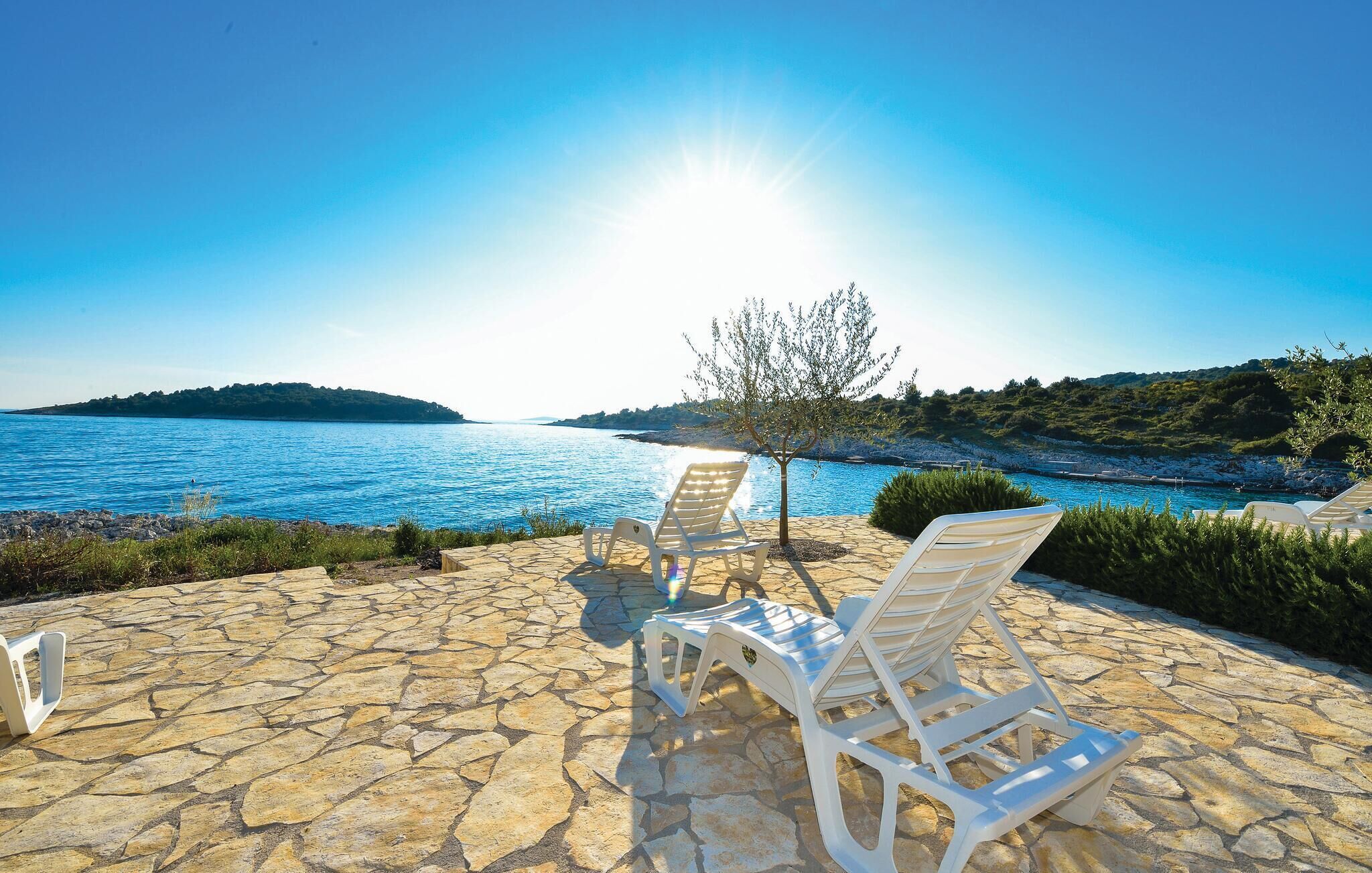 Une terrasse en pierre avec deux chaises longues blanches, donnant sur une étendue d’eau et un arbre.