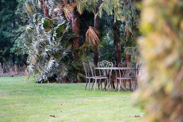 Un espace repas avec une table et des chaises, entouré d’une végétation luxuriante et d’arbres.