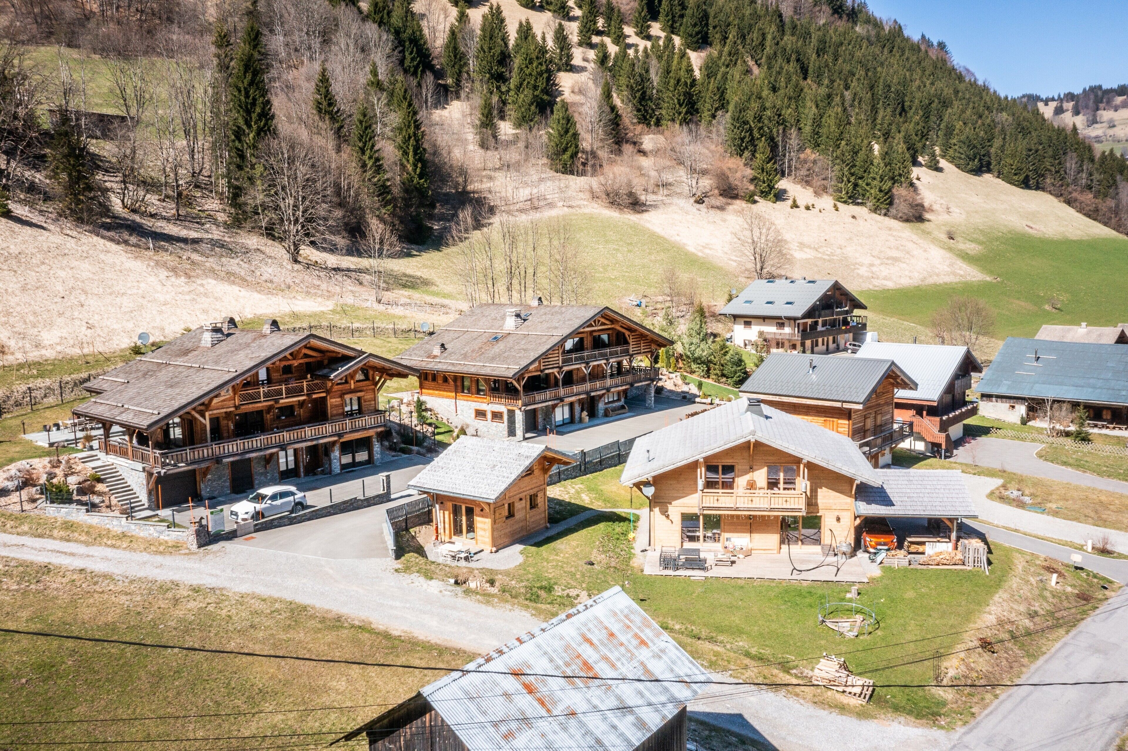 Un chalet comprenant plusieurs cabanes en bois, un bâtiment principal doté d’un balcon, et un paysage environnant composé d’arbres et de collines.