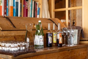 A wooden bar area with various bottles and glasses, a wooden cabinet, and a bookshelf in the background.