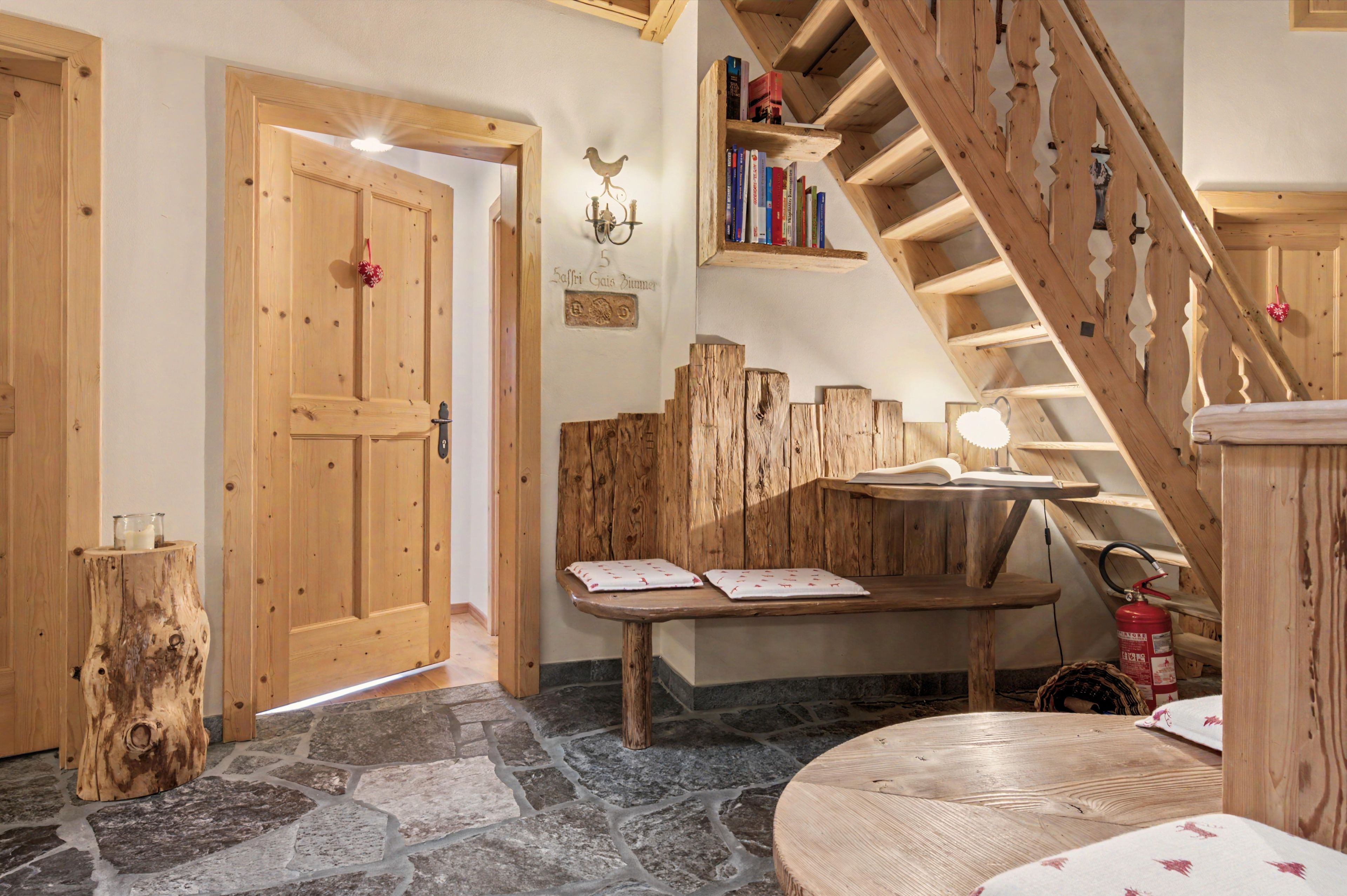Un intérieur en bois avec un plancher en pierre, un escalier en bois, une petite table avec un livre et un extincteur.