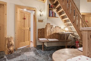 Interior de madera con suelo de piedra, una escalera de madera, una pequeña mesa con un libro y un extintor.
