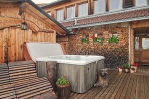 Una cabana de fusta amb un banyera d'hidromassatge, terrassa de fusta i una paret decorada amb plantes i troncs.