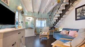 A living room with a blue sofa, a wooden chair, a TV, and a staircase with shelves.