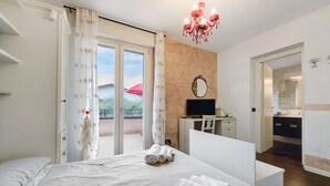 A hotel room with a bed, a desk, a TV, and a balcony with a red umbrella.