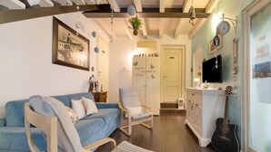 A living room with a blue sofa, a wooden rocking chair, a guitar, and a wall-mounted television.