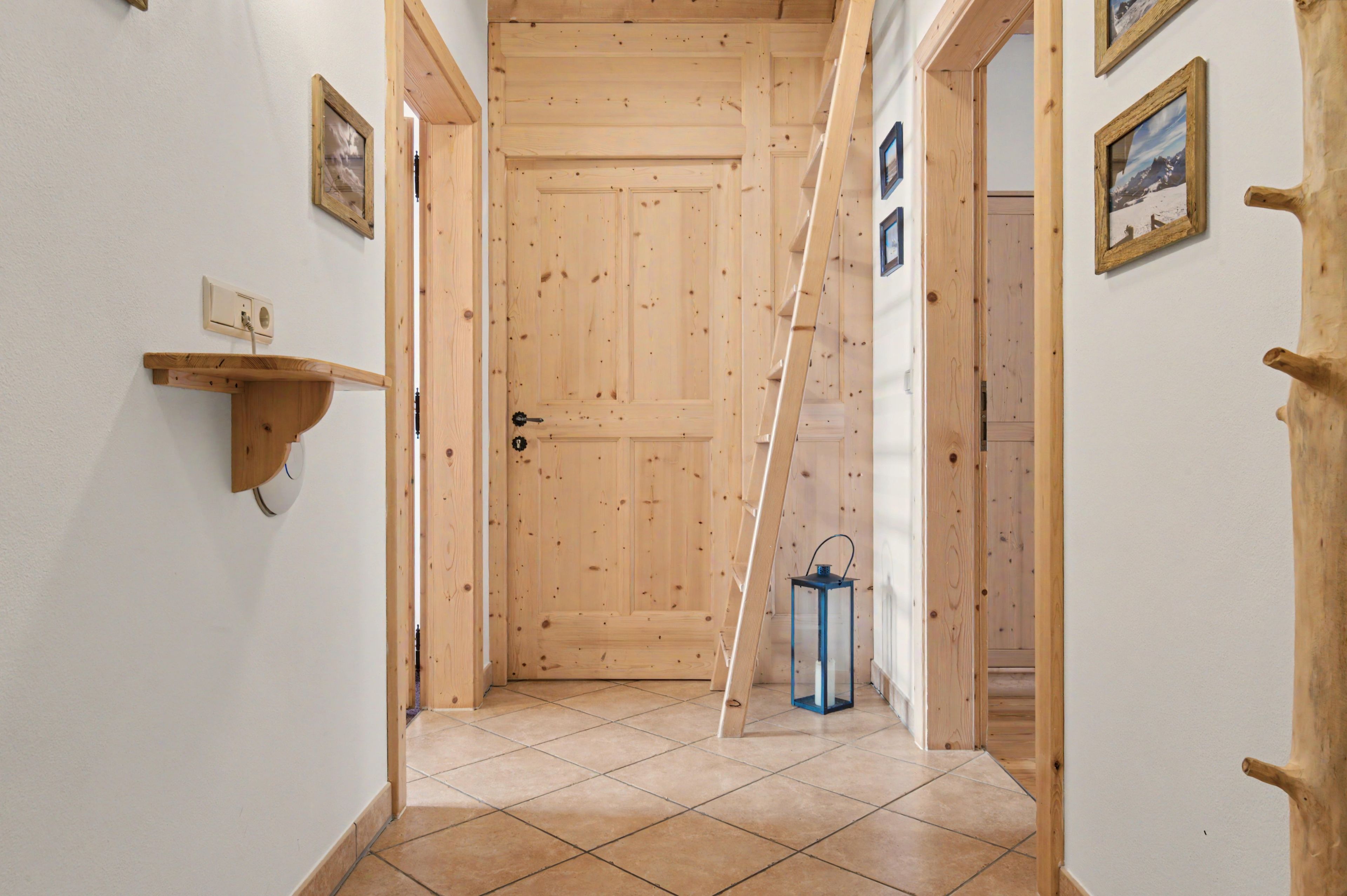Un couloir aux murs en bois, doté d’un sol carrelé, d’une porte, d’une étagère fixée au mur et d’une lanterne.