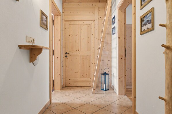 A hallway with wooden walls, a tiled floor, a door, a wall-mounted shelf, and a lantern.