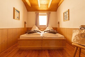 A wooden room with a bed, a window with curtains, and two framed pictures on the walls. - Room 'Rossalm Classic' with Shared Terrace, Shared Garden and Wi-Fi (Brixen)