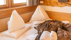 A cozy room with wooden walls, a bed with white pillows, a blanket, and a wooden headboard. - Room 'Rossalm Classic' with Shared Terrace, Shared Garden and Wi-Fi (Brixen)