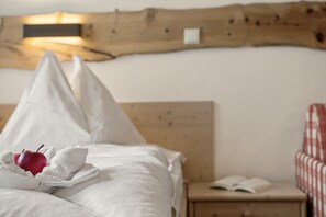 A bed with white linens, a red apple, and a towel. There is a wooden headboard and a small bedside table with an open book.