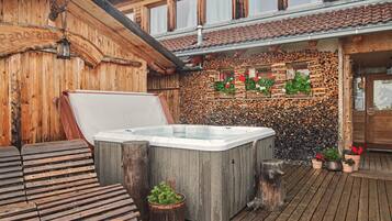 A wooden cabin with a hot tub, wooden deck, and a wall decorated with plants and logs.