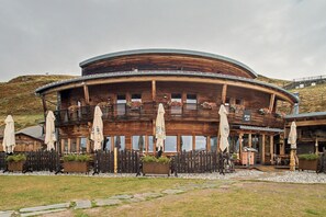 A wooden building with a circular design, featuring outdoor seating with umbrellas and flower arrangements.