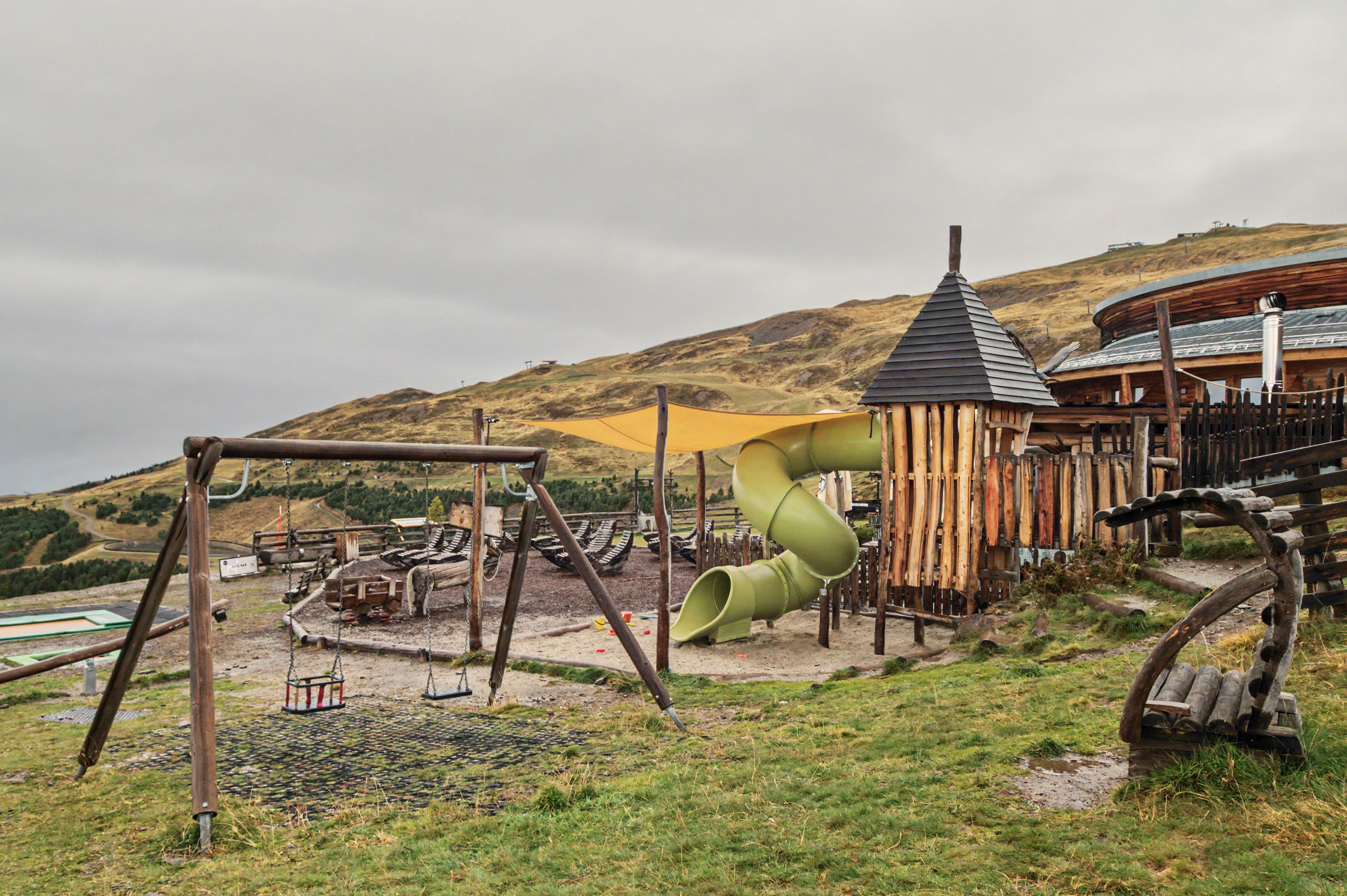 A playground with a slide, swings, and a wooden playhouse.