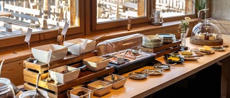 Een buffetopstelling met diverse gerechten, bestek en houten meubilair, met zicht op een stadsgezicht door grote ramen.