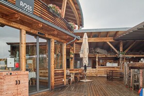 A wooden building with a covered patio area, large windows, and outdoor seating.