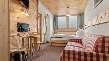 A cozy room with a bed, a wooden table with chairs, a television, and a window with curtains.