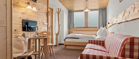 Una habitación acogedora con una cama, una mesa de madera con sillas, un televisor y un ventanal con cortinas.