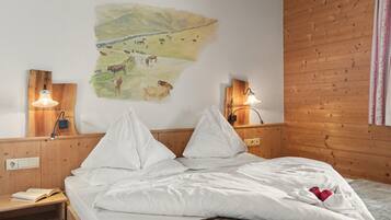 Quarto com cama, duas mesas de cabeceira, luminária na parede e pintura de vacas em uma fazenda.
