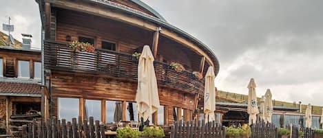 A wooden building with a curved roof, outdoor seating with umbrellas, and a gravel pathway.