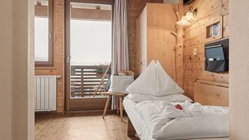 Quarto de cabana de madeira com cama, cadeira, janela com cortinas e luminária na parede.