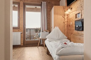 Ein Zimmer in einer Holzhütte mit einem Bett, einem Sessel, einem Fenster mit Vorhängen und einer Wandleuchte.