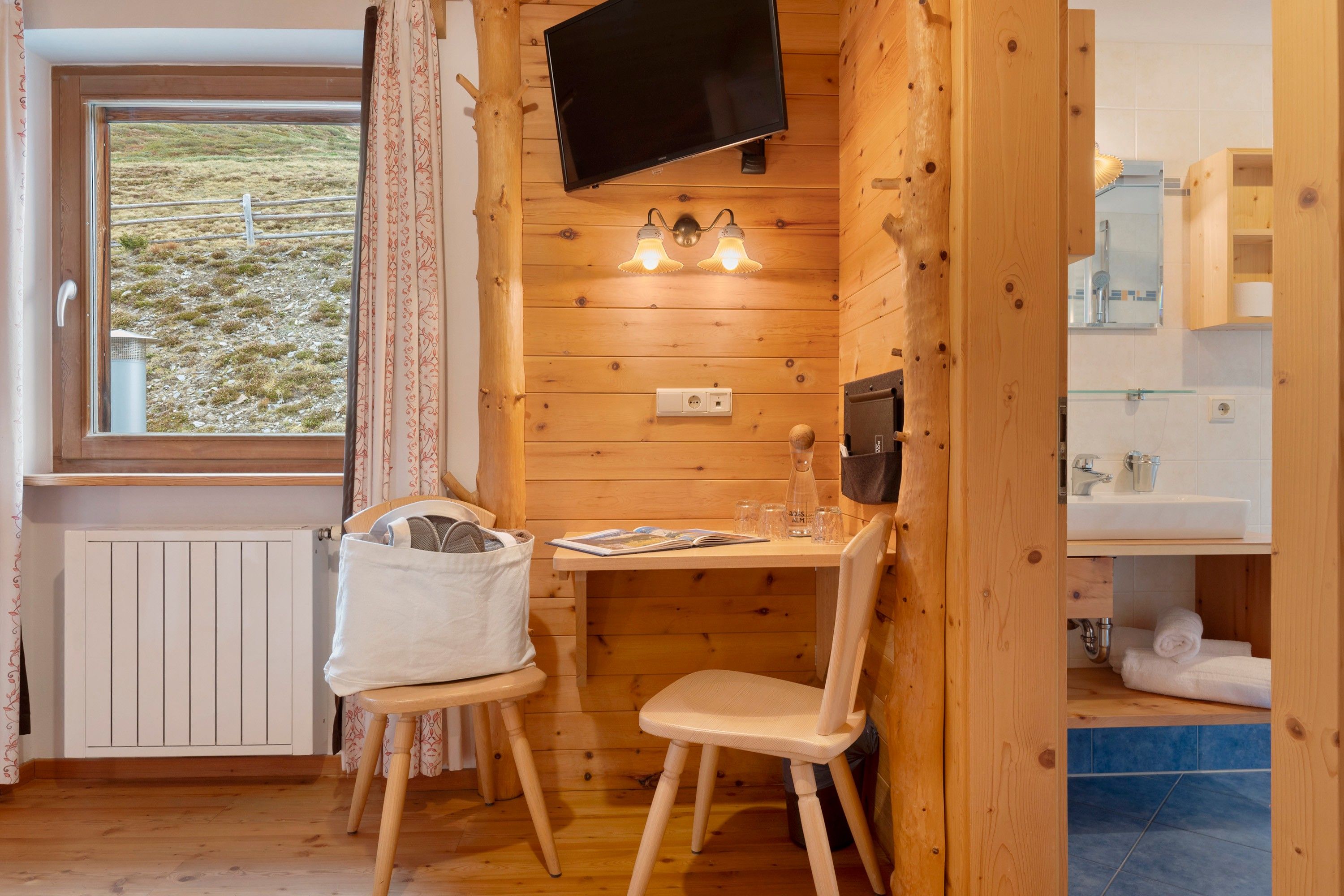 Ett mysigt stugrum med träpanel på väggarna, en tv som hänger på väggen, ett bord med stolar och ett fönster med gardiner.