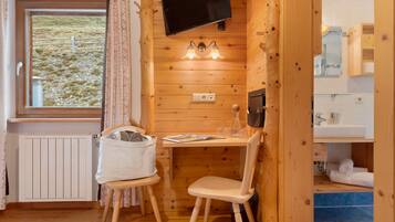 Ett mysigt stugrum med träpanel på väggarna, en tv som hänger på väggen, ett bord med stolar och ett fönster med gardiner.