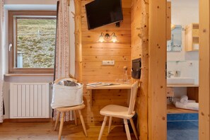 Habitació d'un càbana acollidora, amb interior de fusta, un televisor fixat a la paret, una taula amb cadires i una finestra amb cortines.