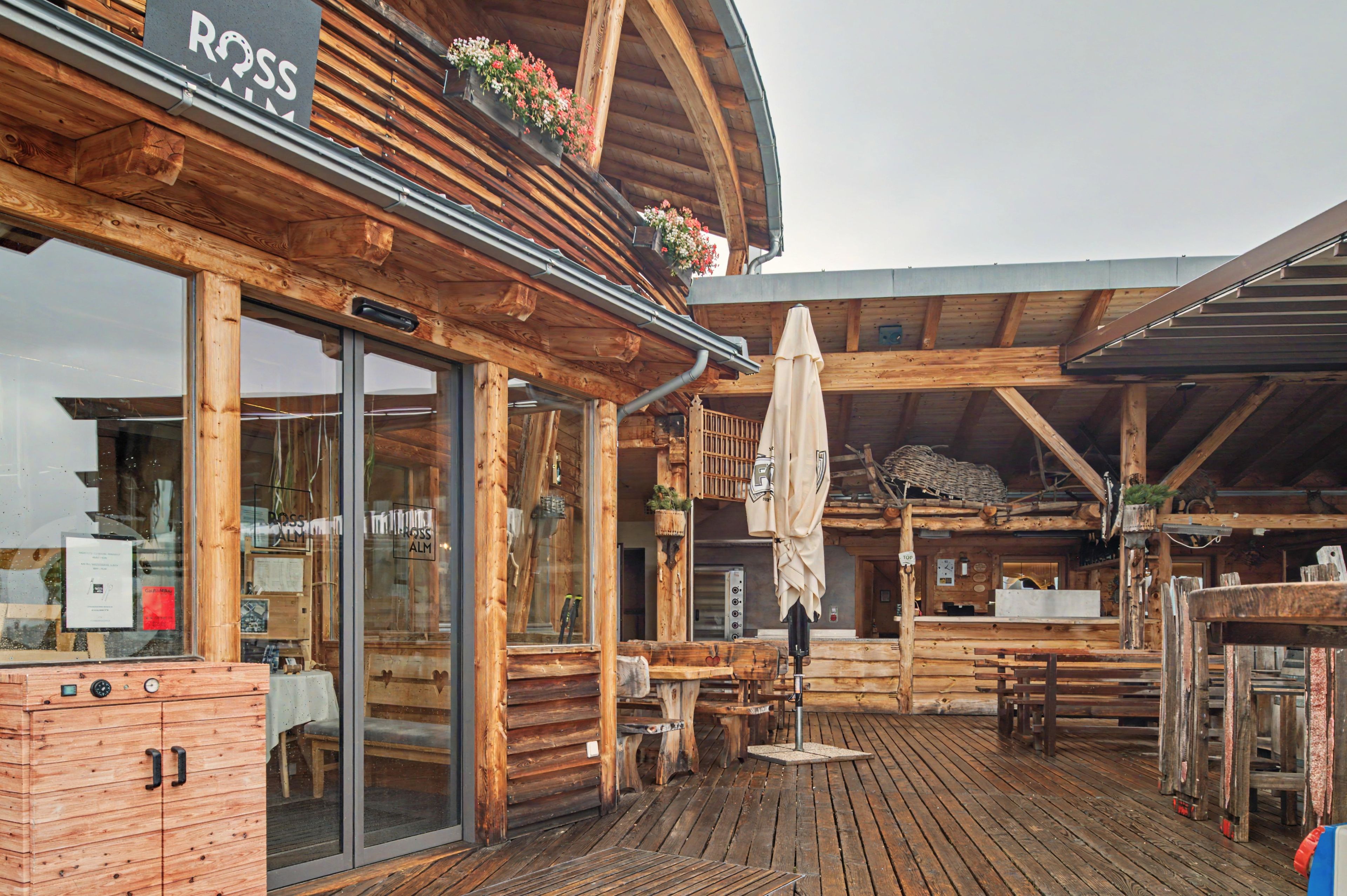 Ein Holzhaus mit überdachter Terrasse, großen Fenstern und Sitzgelegenheiten im Freien.