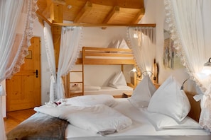 Een slaapkamer met een stapelbed, witte lakens, kantgordijnen en een houten plafond.