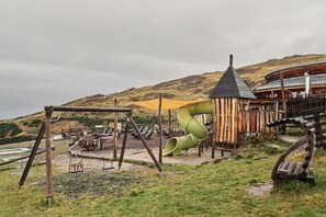 A playground with a slide, swings, and a wooden playhouse. - Room 'Four-Poster Bed Room' with Shared Terrace, Shared Garden and Wi-Fi (Brixen)