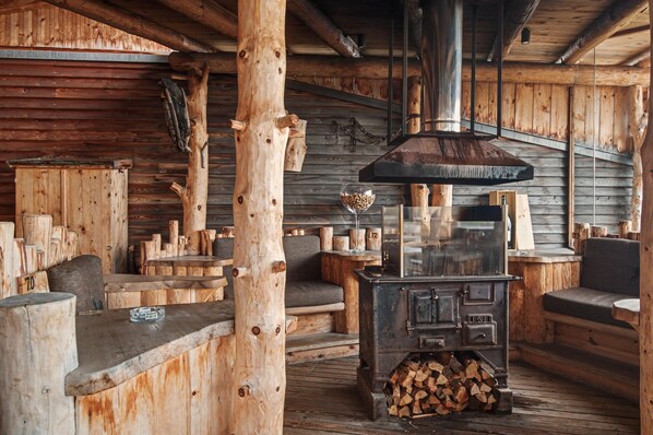 A rustic wooden interior with a large wood-burning stove, benches, and a glass-top table.