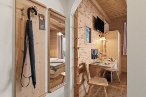 A wooden interior with a bed, a desk, and a chair. There is a coat rack with a coat and a sign that says 'PLEASE CLEAN UP MY ROOM.' - Room 'Rossalm Panoramic Room 3' with Shared Terrace, Shared Garden and Wi-Fi (Brixen)