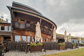 Un edificio de madera con techo curvo, mobiliario exterior con sombrillas y un camino de grava.
