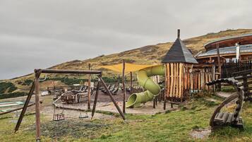Ein Spielplatz mit Rutsche, Schaukeln und einem Spielhäuschen aus Holz.
