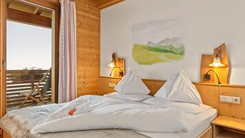 Ein Zimmer einer Holzhütte mit einem Bett, einem Fenster mit Vorhängen und einer Wandlampe.