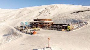 Une montagne enneigée, avec un bâtiment en bois, des remontées mécaniques et une piste de ski.