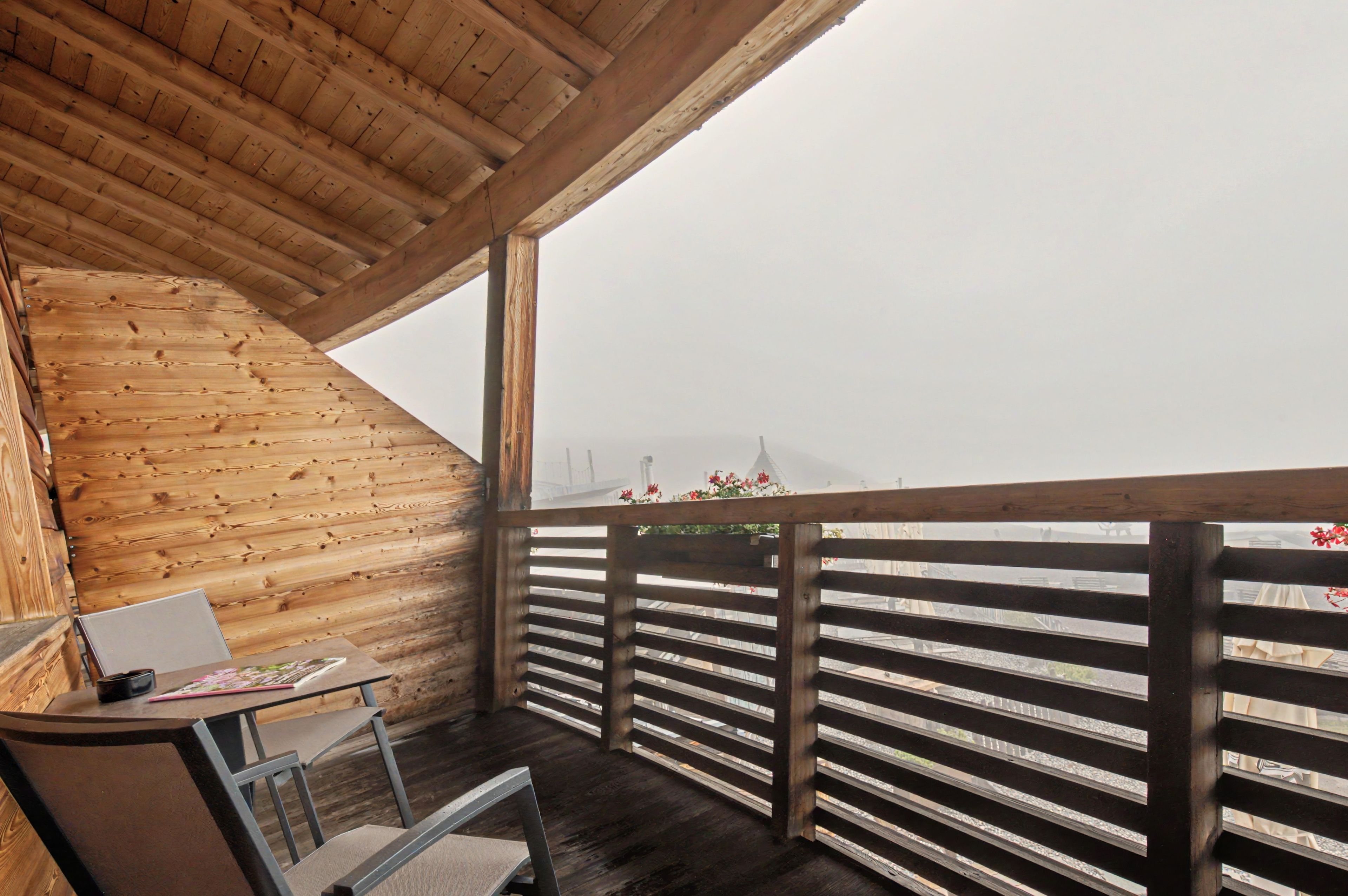 Une cabane en bois dotée d’un balcon donnant sur un paysage brumeux.