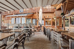 Een rustiek houten interieur met meerdere houten tafels en banken, een bordje met de tekst 'ROSS ALM' en een overdekt terras.