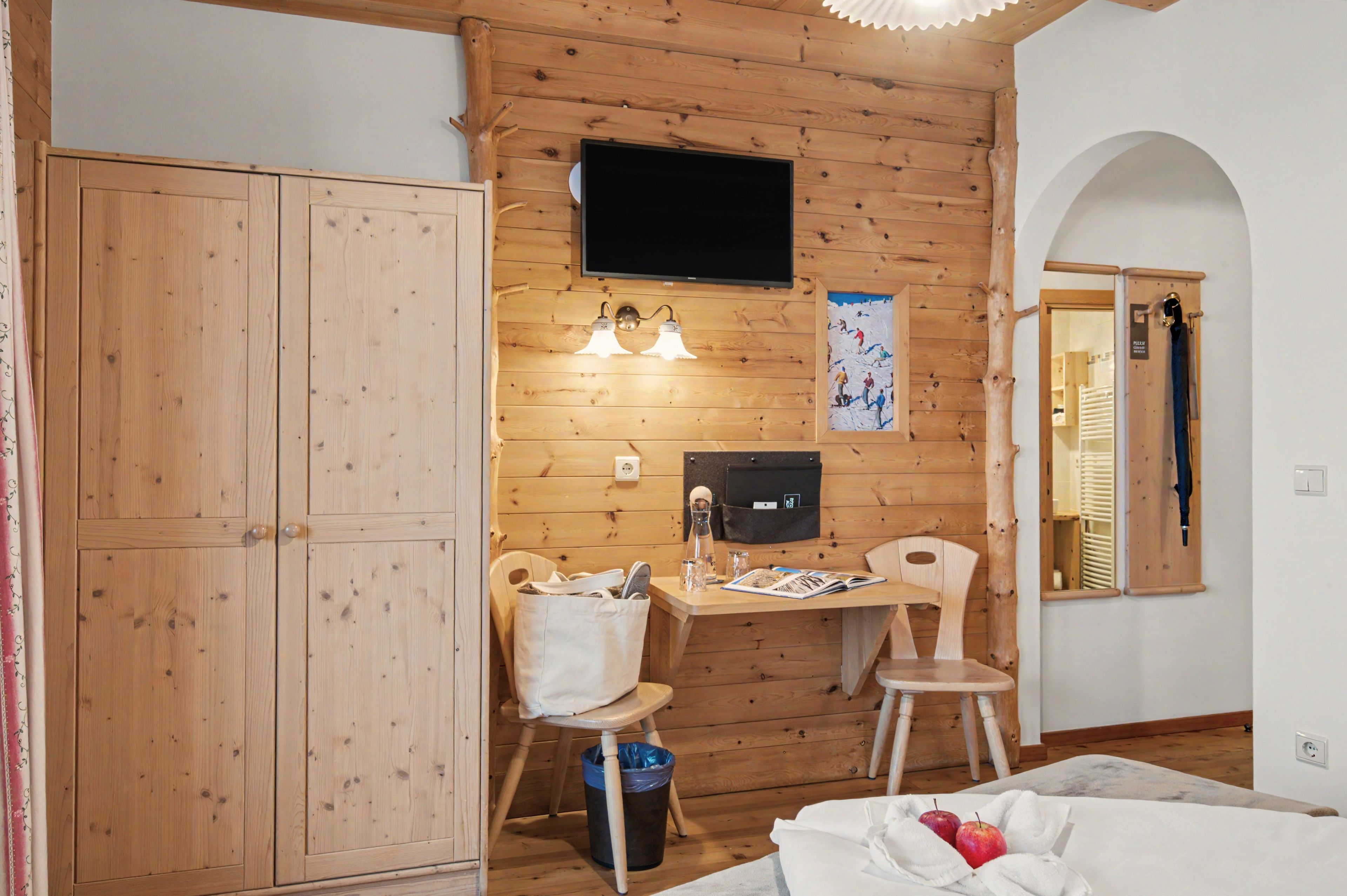 Quarto com painéis de madeira, uma escrivaninha, cadeira, televisão e um guarda-roupa grande.