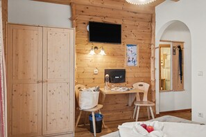 Een kamer met houten lambrisering, een bureau, stoel, televisie en een grote kledingkast.