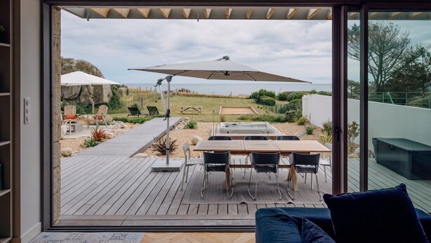 A modern patio with a table and chairs, a large umbrella, and a view of the ocean. - La Perle, 6 guests, 180° sea view, jacuzzi (Plobannalec-Lesconil)