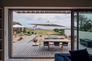 Un patio moderno con una mesa y sillas, un parasol grande y vistas al océano.