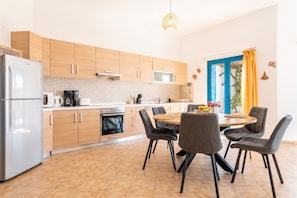 A modern kitchen with wooden cabinets, a stainless steel refrigerator, a microwave, and a dining area with a round table and chairs. - Holiday Home 'Kalliope' with Sea View, Wi-Fi and Air Conditioning (Gennadi - Rhodos - Dodekanese)