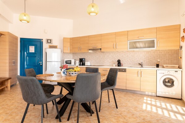 A modern kitchen with wooden cabinets, a blue door, a dining table with chairs, a washing machine, and a microwave. - Holiday Home 'Kalliope' with Sea View, Wi-Fi and Air Conditioning (Gennadi - Rhodos - Dodekanese)